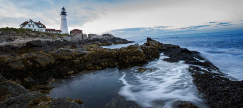 A view of the ocean waves crashing against the coastline and the Cape Elizabeth Lighthouse