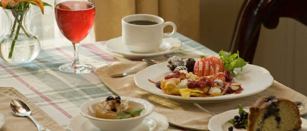 A glass of juice, cup of coffee, an entreé plate, a bread plate, and a bowl all containing breakfast food sit atop a table at Berry Manor Inn.