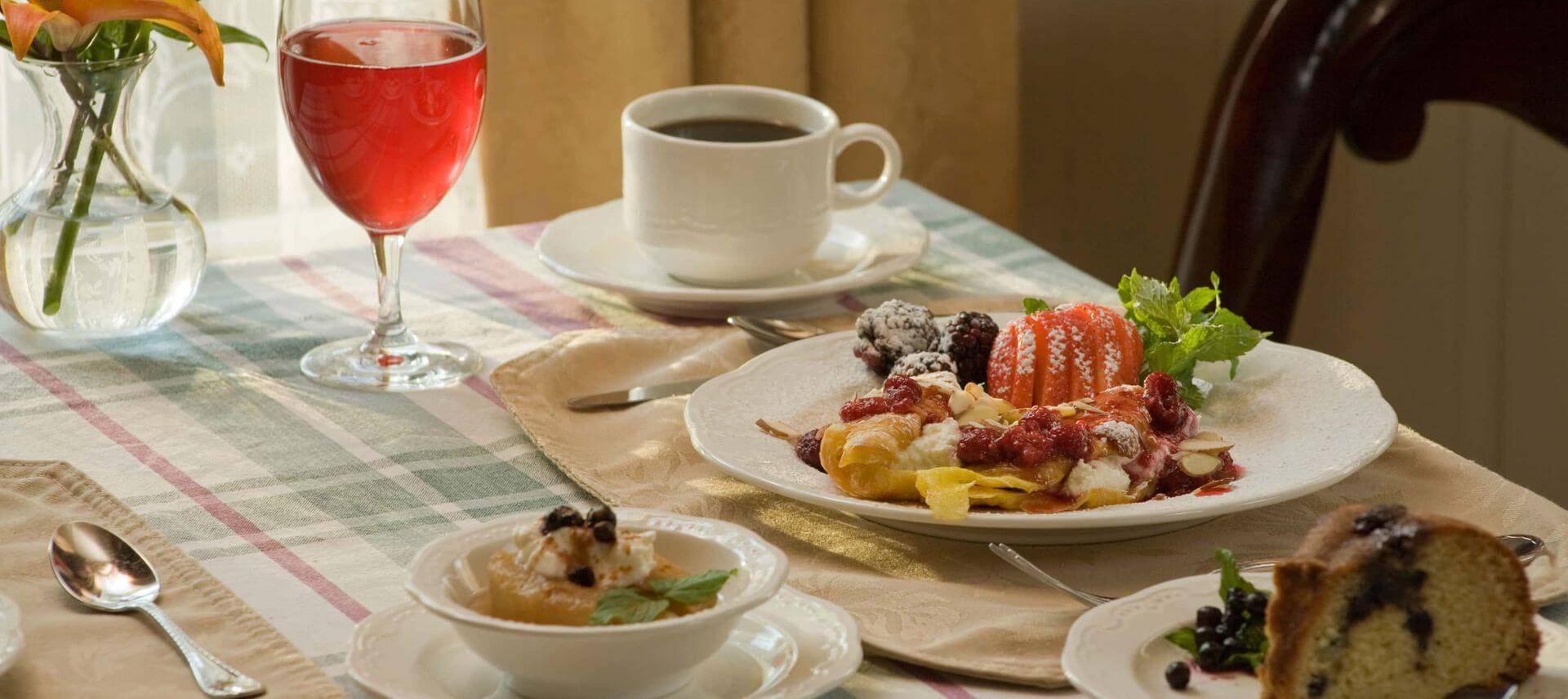 A glass of juice, cup of coffee, an entreé plate, a bread plate, and a bowl all containing breakfast food sit atop a table at Berry Manor Inn.