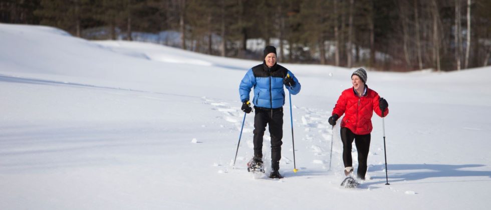 A couple holding poles are snowshoeing outside