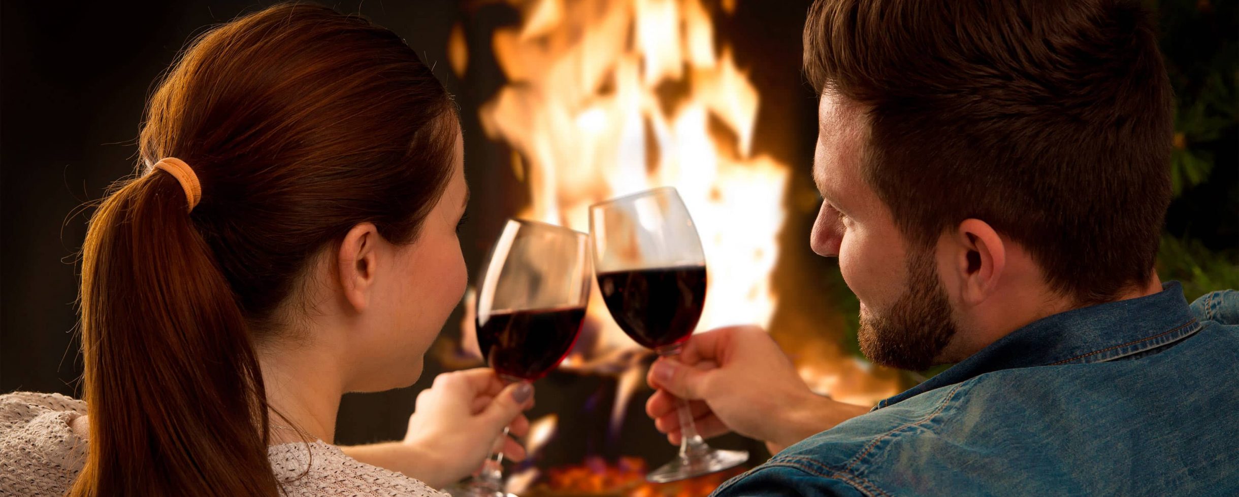 Couple toasting red wine in front of fireplace