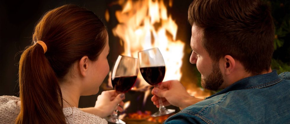 Couple toasting red wine in front of fireplace