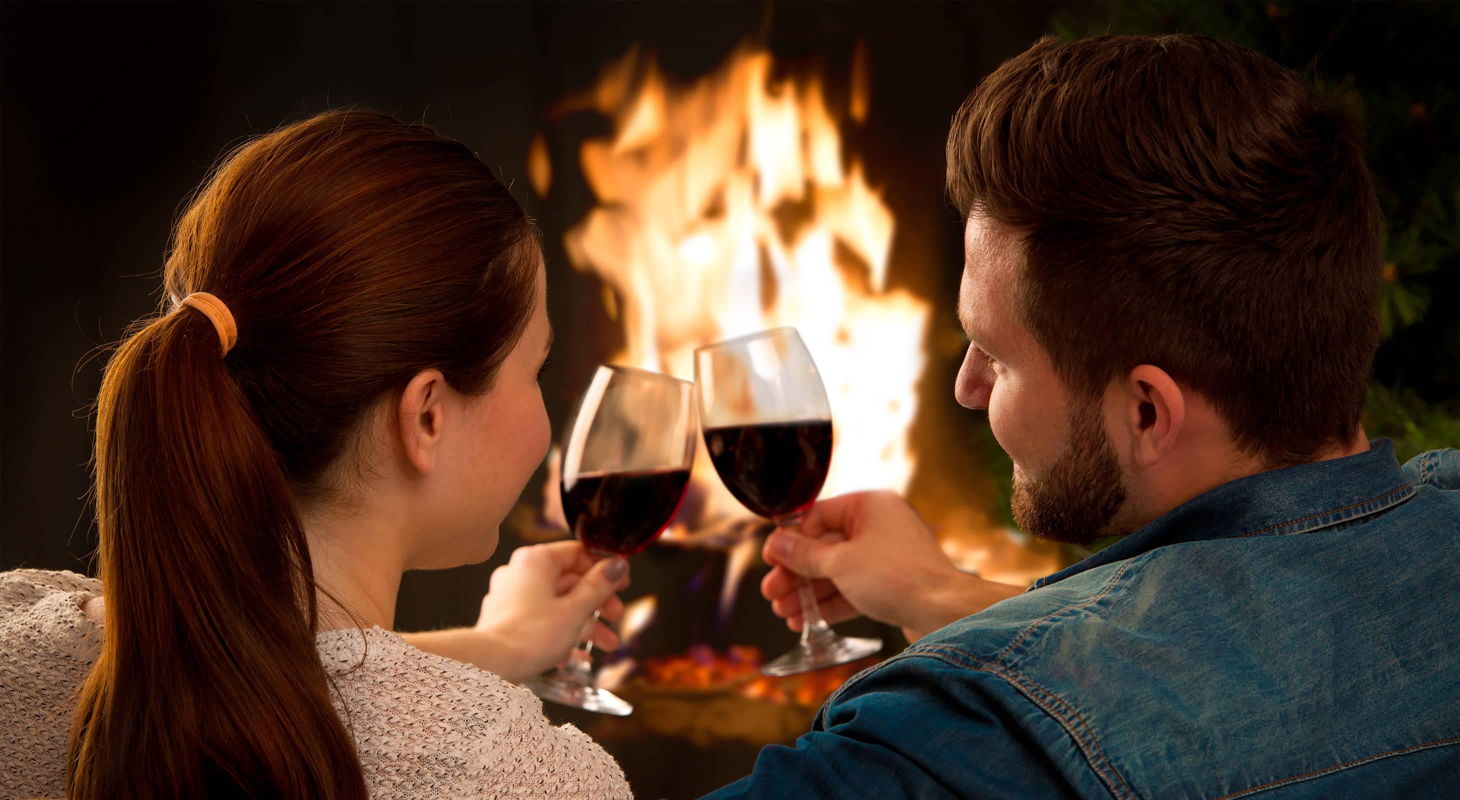 Couple toasting red wine in front of fireplace