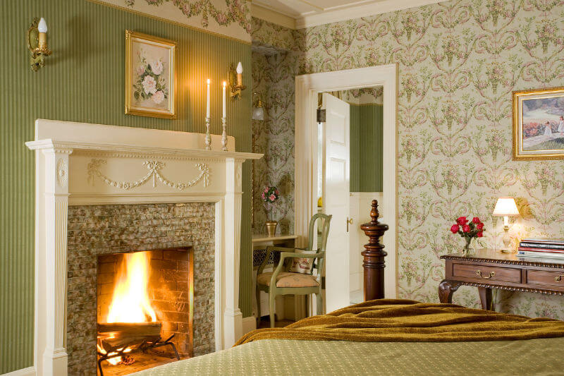 Romantic guest room with sage green walls and a raoring fire in the fireplace