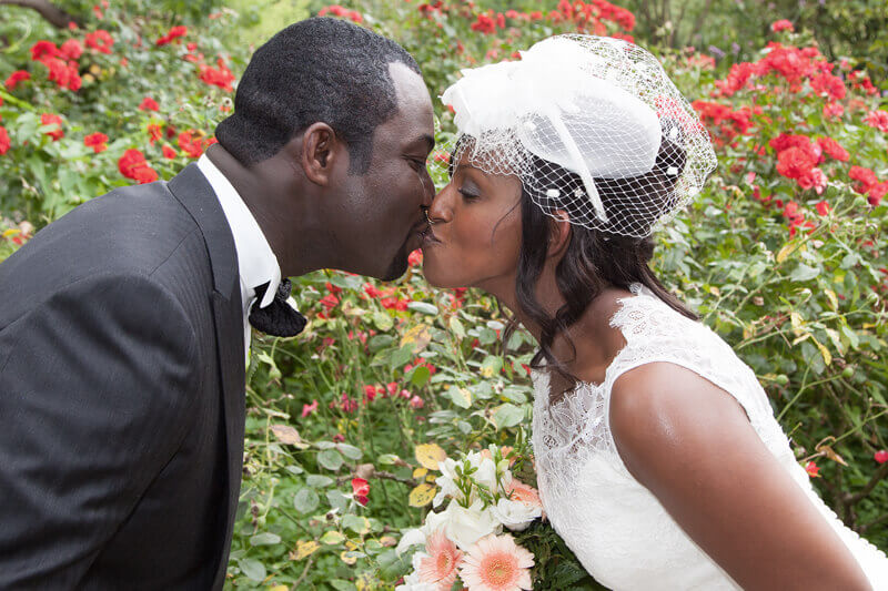 African American couple kissing in the rose garden on their wedding day