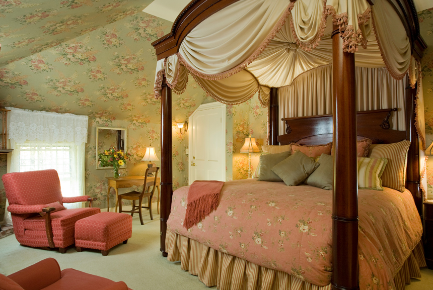 A hand carved mahogany four-poster custom king canopy bed draped in flowing swags of silk fabric is the centerpiece for this luxury room to celebrate an anniversary at the Berry Manor. 