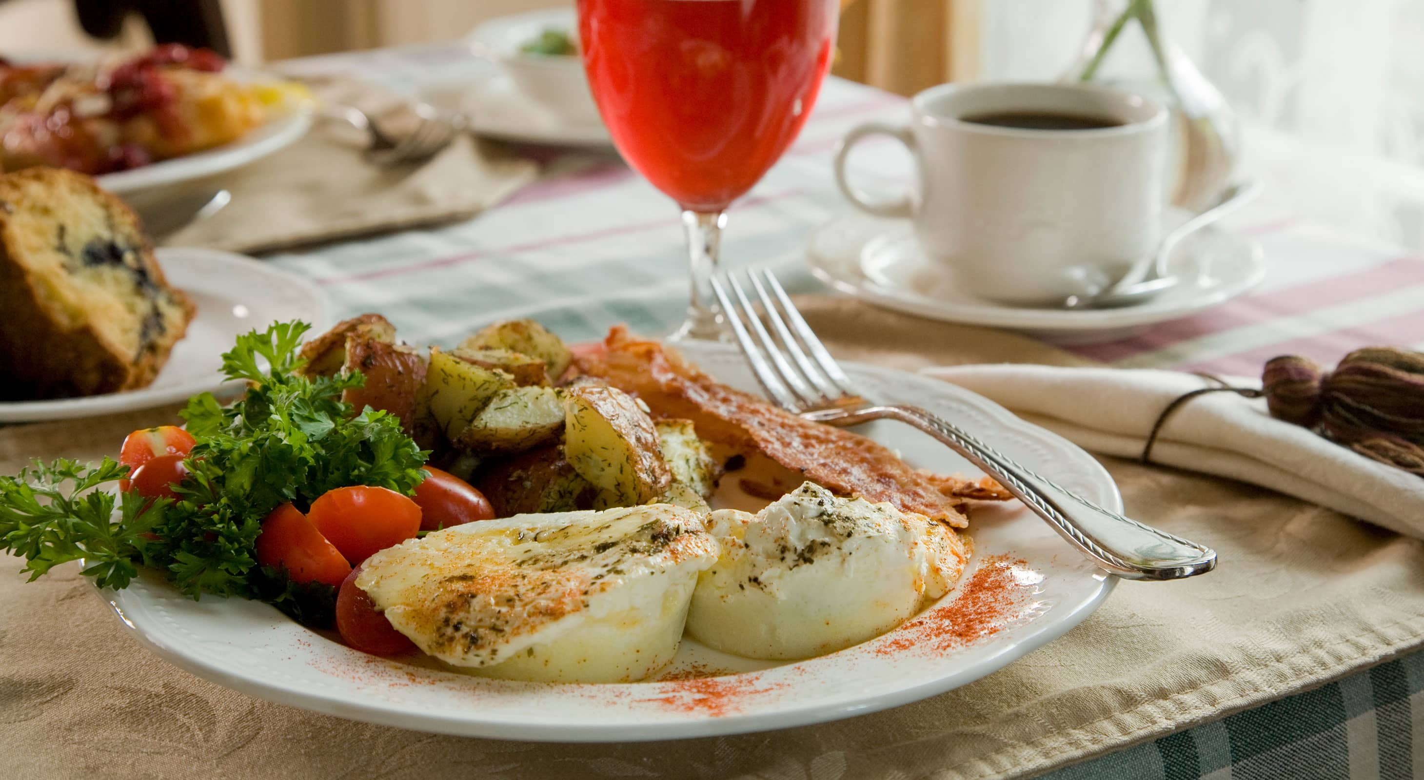 Plate with egg dish, greens, and bacon next to juice glass