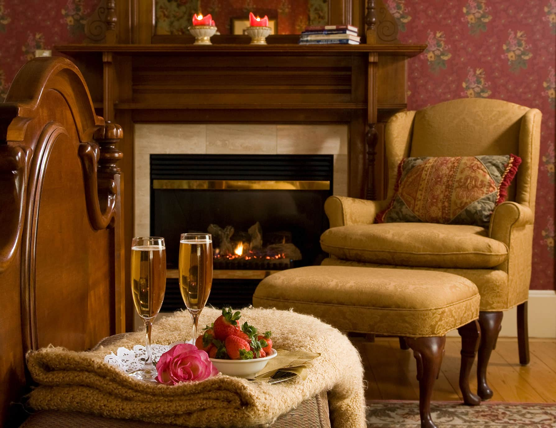 Chest at the foot of ornate bed by fireplace with chair