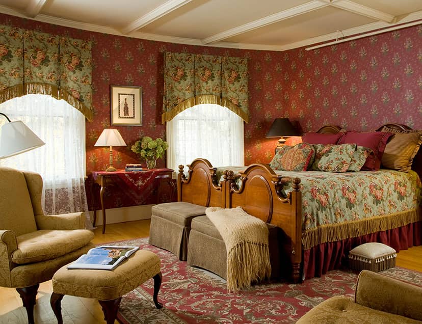 Room with ornate large bed across from sitting area and tall windows