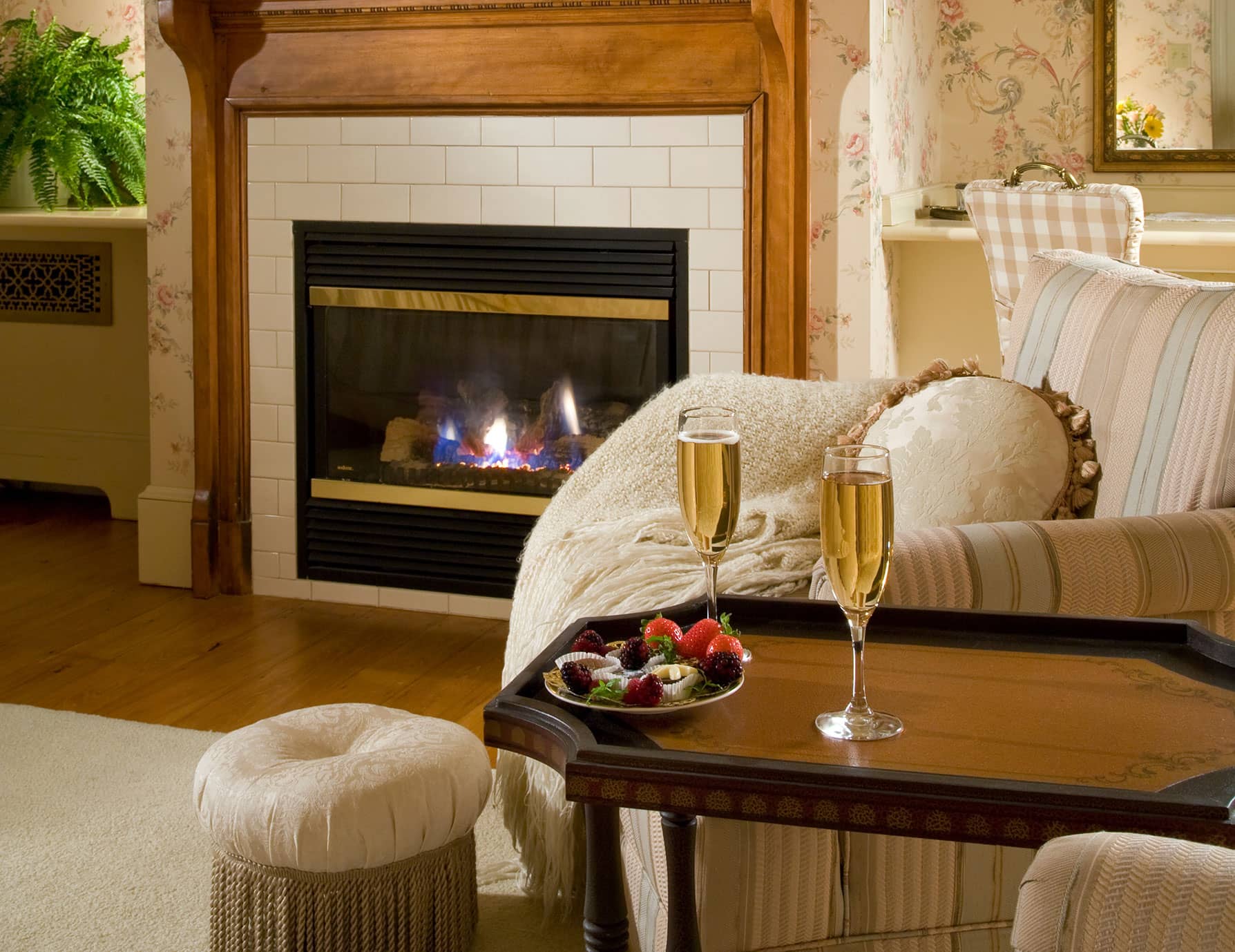 Champagne glasses by chocolate-covered strawberries on sitting area table by fireplace