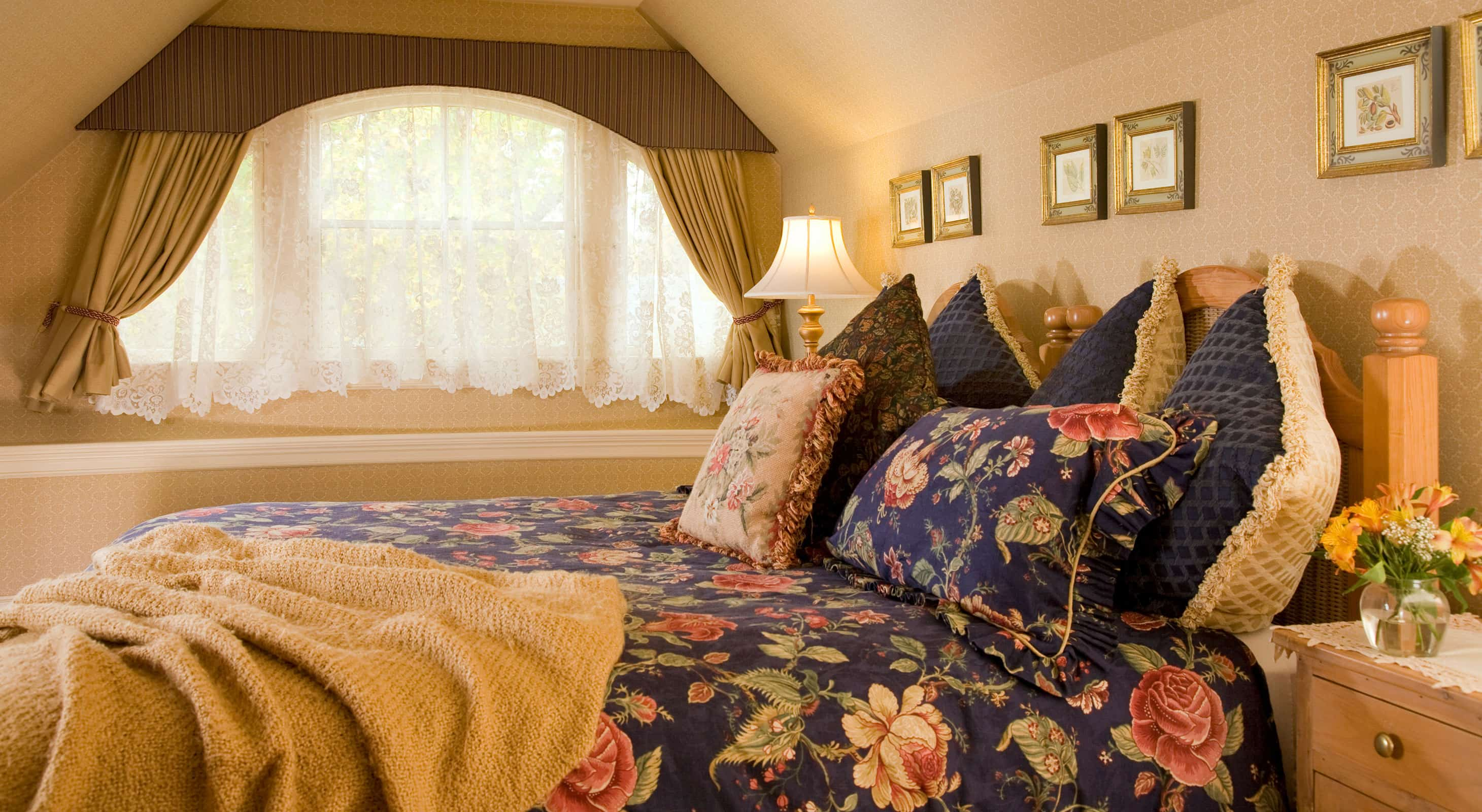 Plush bed with many pillows across from tall window in Room 5