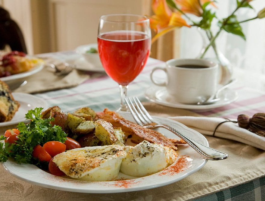 Egg breakfast with bacon, potatoes, and greens on plate next to juice and coffee mug