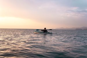 Sole kayaker at dusk paddling on the ocean with a pink and yellow tinged sky