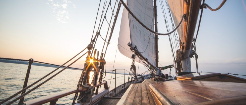 View from the deck of a sailboat soaring through the open water with full white sails