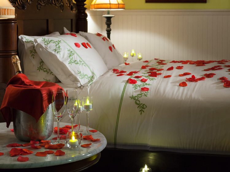 Red rose petals strwn across a bed with with down comforter.