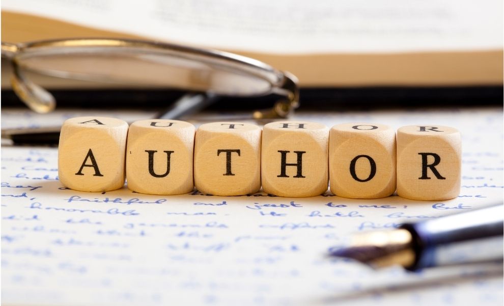 Scrabble letters that spell out author sitting on a handwritten draft with a book nearby.