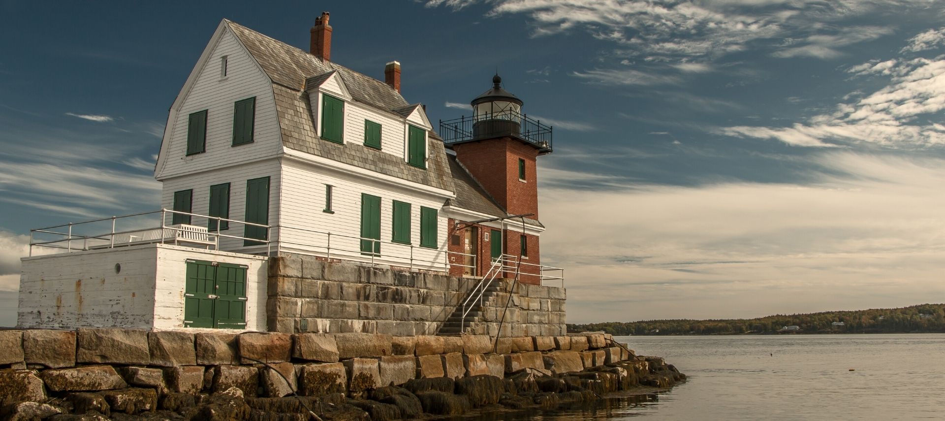 Beautiful red lighthouse with attached two-story white house on a rocky outcropping overlooking the water
