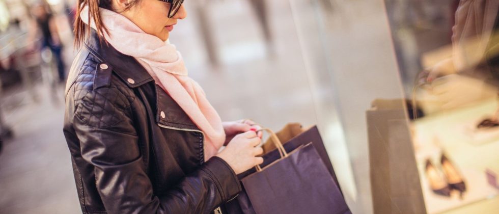 A woman with pink scarf holding bags while window shopping