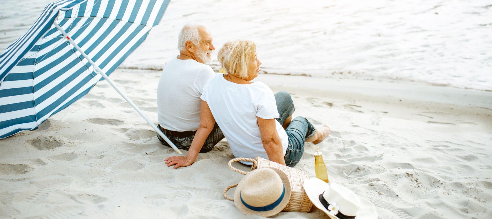 An older couple sitting on the beach under a beach umbrella
