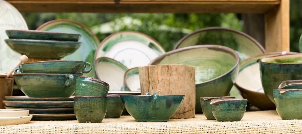 A display of green glazed wheel-thrown pottery for sale. Assorted cups, plates, and bowls.