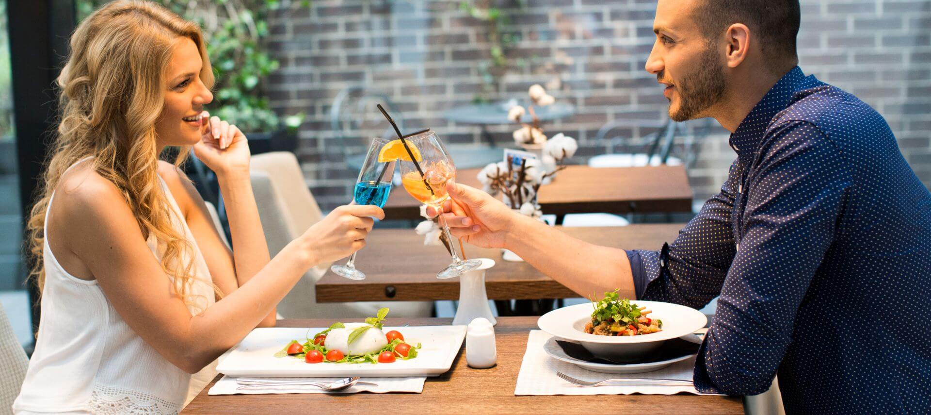 A couple doing cheers with drinks while eating at a restaurant