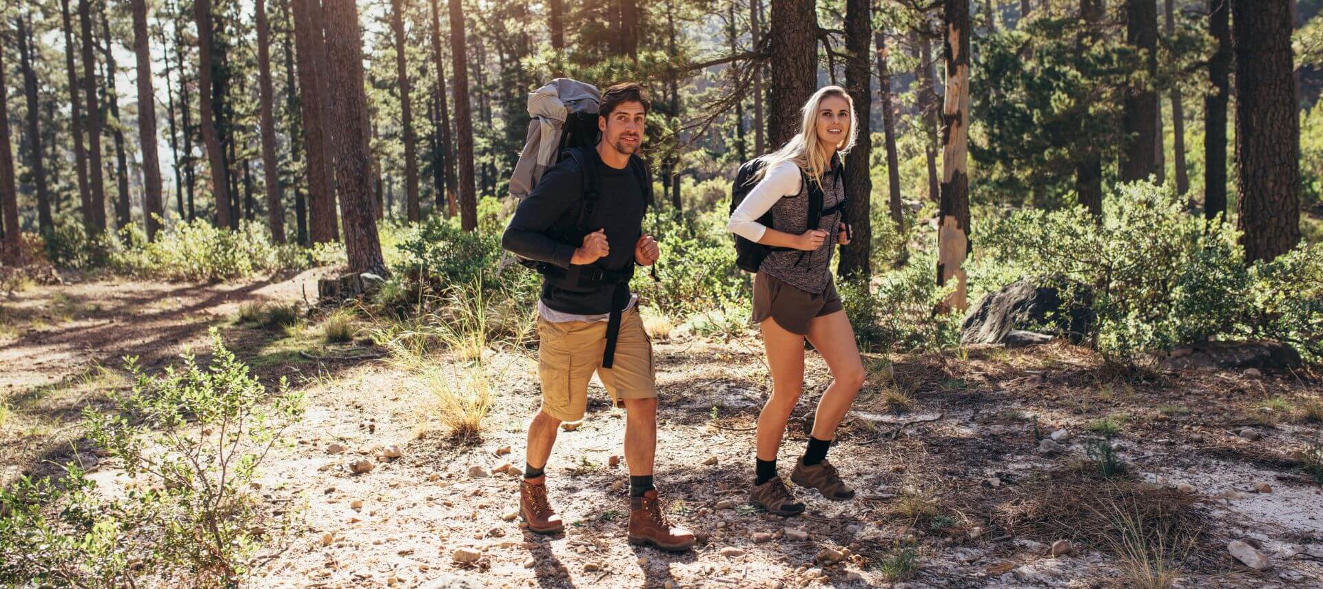 A couple is hiking with backpacks in the woods