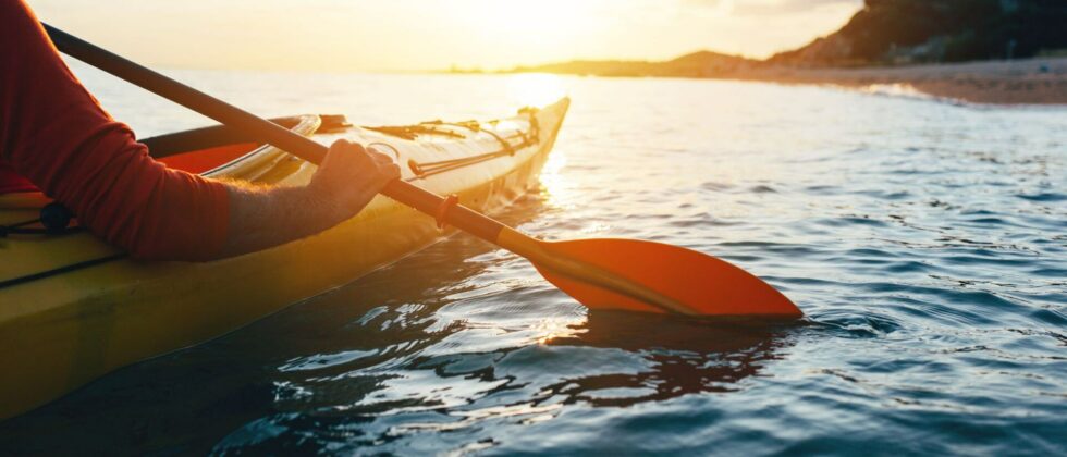 A person sea kayaking at sunset with a view of the shore in the distance