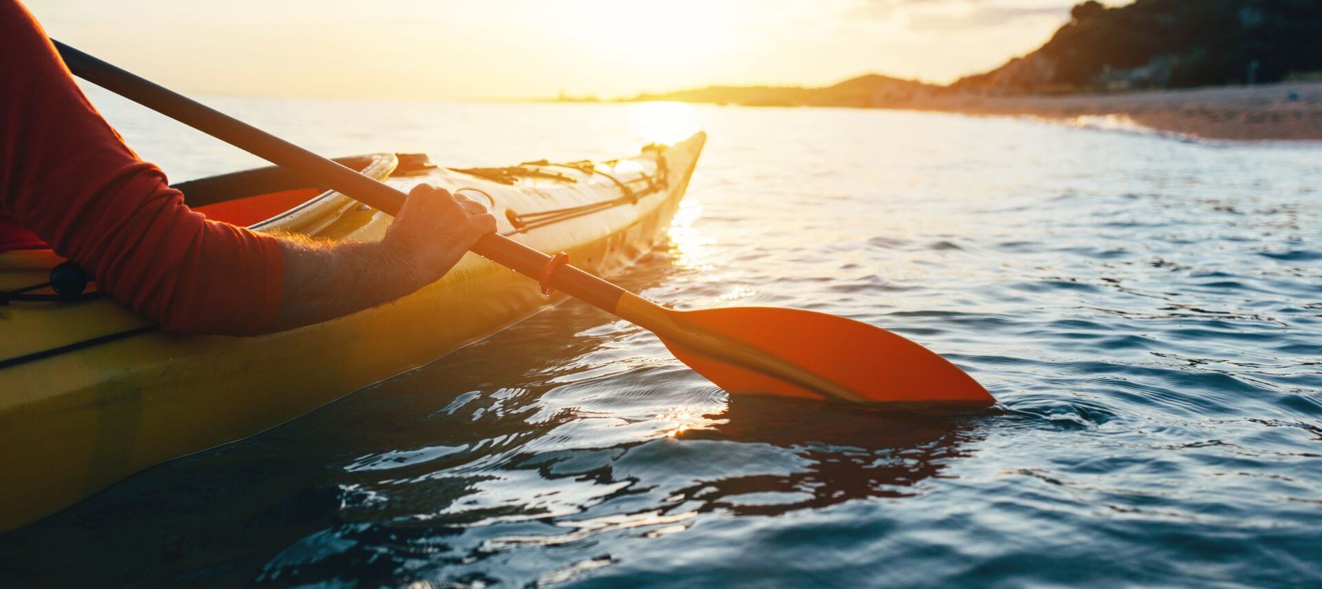 A person sea kayaking at sunset with a view of the shore in the distance